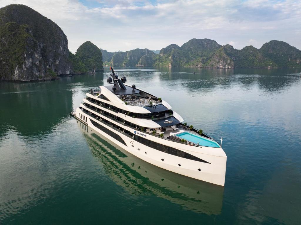 a yacht in the water with mountains in the background at Victorious Cruise Ha Long Bay in Ha Long
