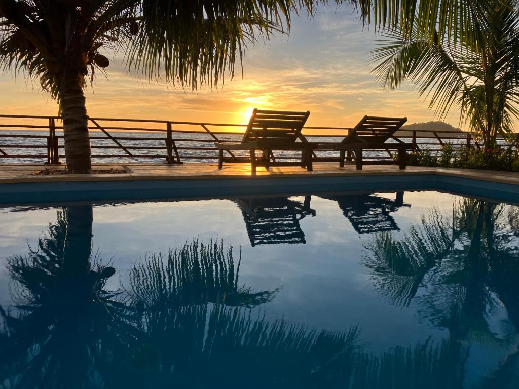 two benches sitting next to a swimming pool with the sunset at Villa MAYANKI in Dzamandzar