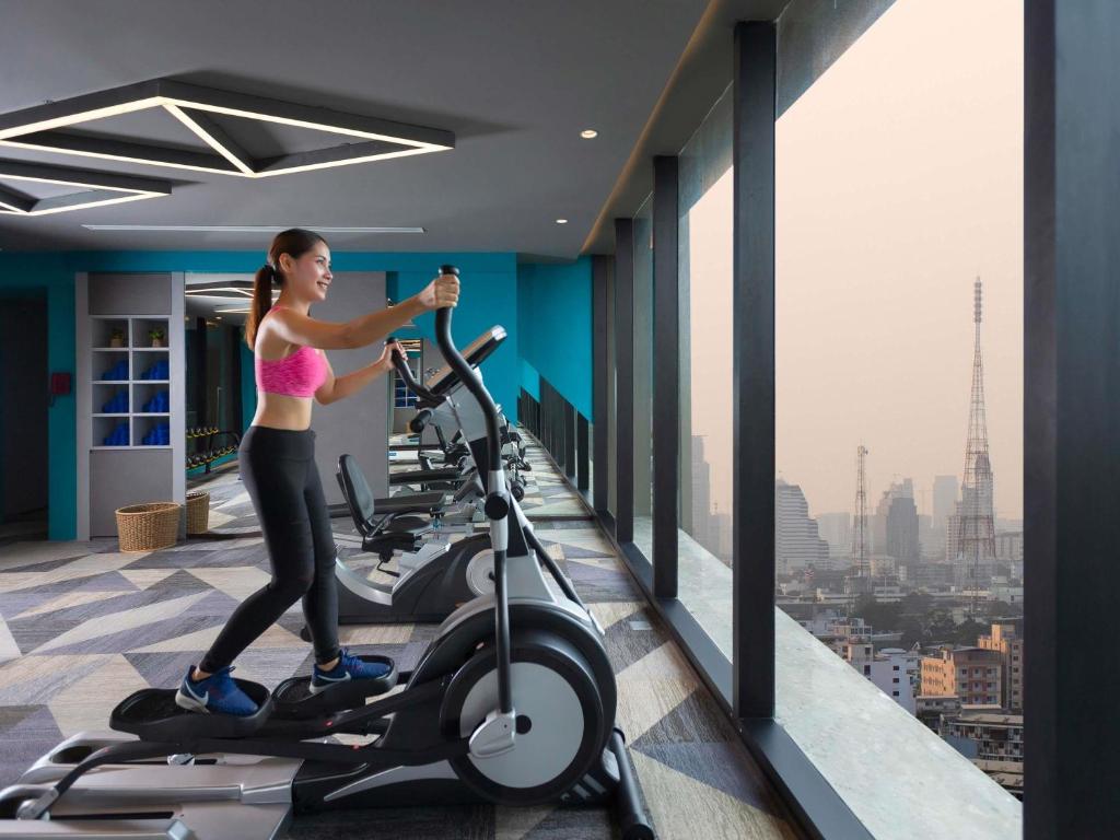 A bright gym with cardio machines facing a Bangkok city view.