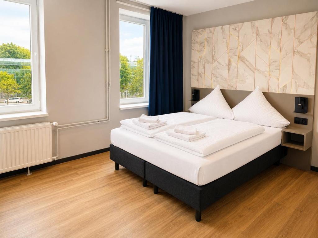 a bedroom with a bed with white sheets and two windows at Nivara Hotel in Hamburg
