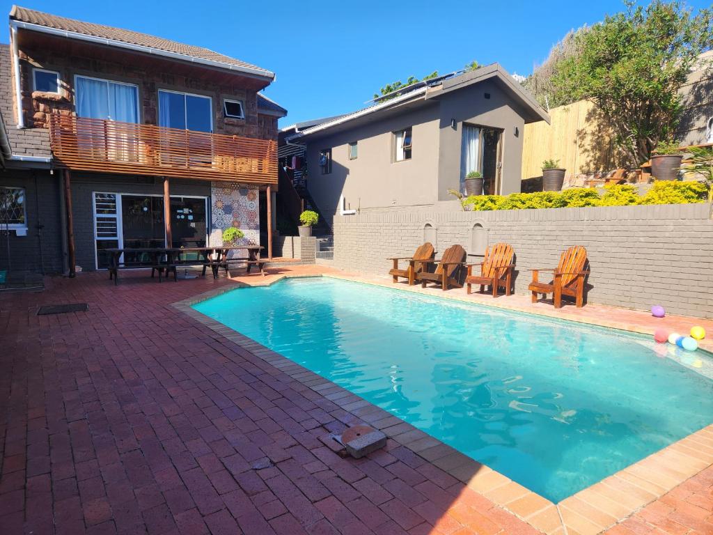 a swimming pool with chairs and a house at Lungile Backpackers in Gqeberha