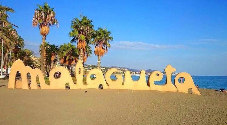 a sign on a beach with palm trees in the background at M-Room in Málaga