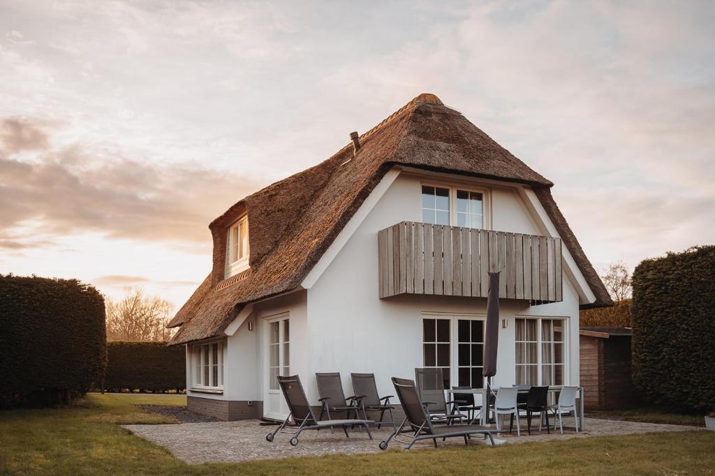 a white house with a thatched roof and chairs at Dutchen Waddenduyn in Den Burg