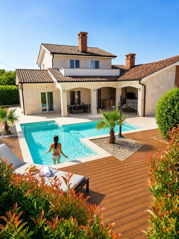 a woman in a swimming pool in front of a house at Villa Adeline in Sveti Ivan Dobrinjski