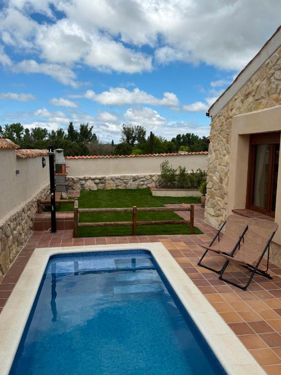 a swimming pool with a chair and a house at Casa Rural Belladona in Valdeprados