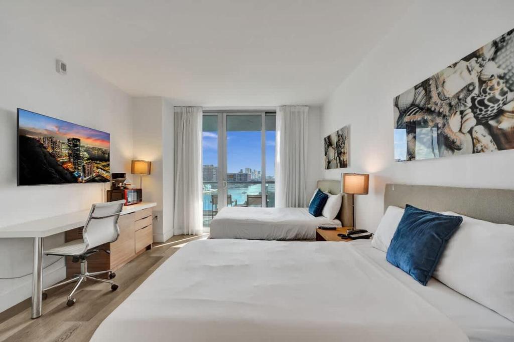 a bedroom with two beds and a desk with a computer at Charming Studio by the Ocean Beach Service in Hallandale Beach