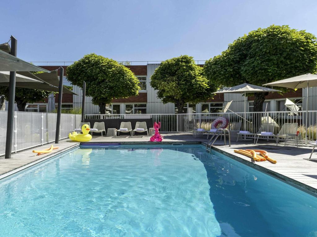 a swimming pool with chairs and umbrellas at Novotel Lyon Bron in Bron