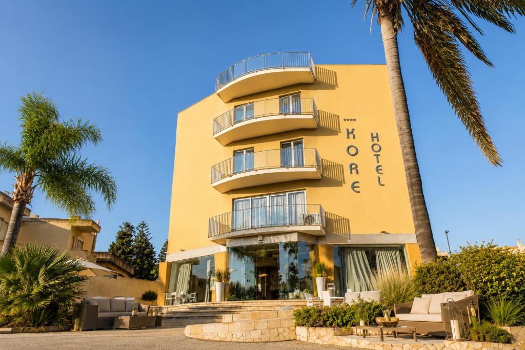 a yellow building with palm trees in front of it at Hotel Kore in Villaggio Mosè