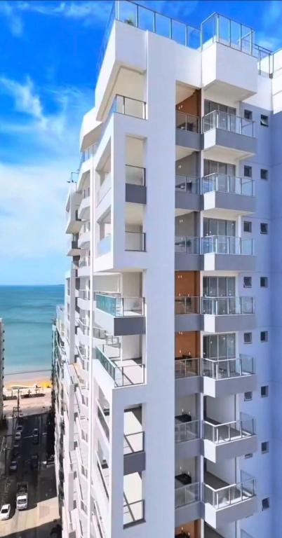 a tall white building with the beach in the background at Apartamento Confortável na Praia do Morro in Guarapari