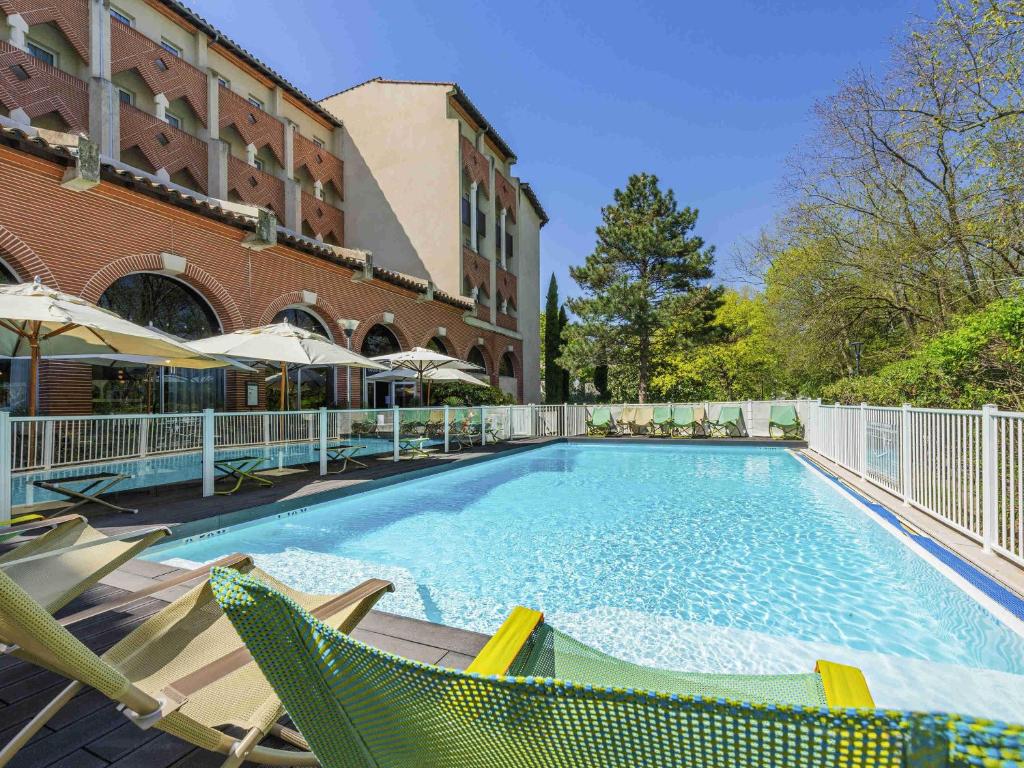 a large swimming pool with chairs and a building at Novotel Toulouse Centre Compans Caffarelli in Toulouse