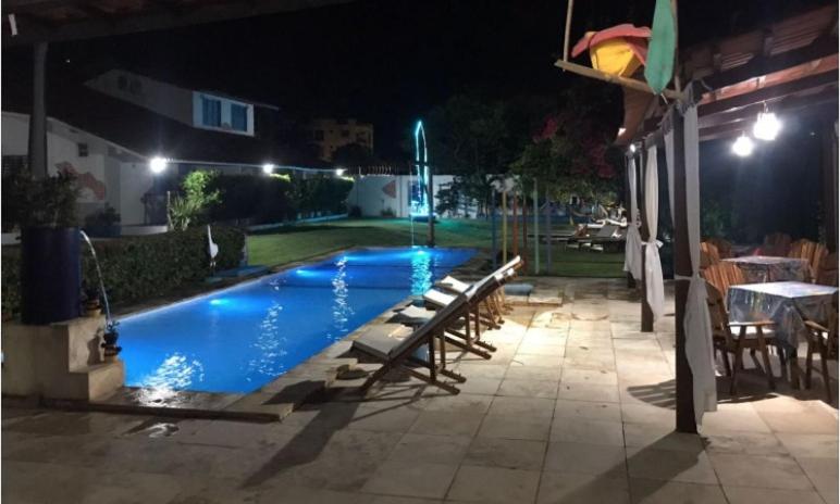 a swimming pool at night with chairs and a table at Pousada 3 Abelhas in Caucaia