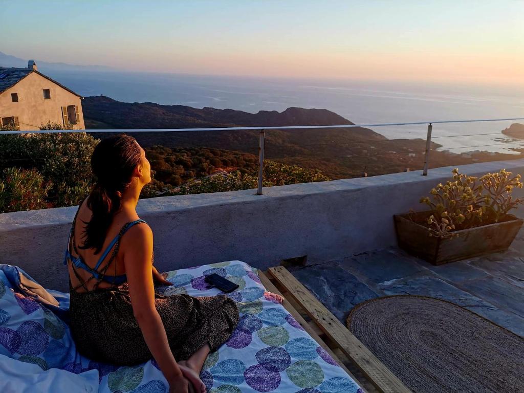 a woman sitting on a bed looking at the sunset at Chambre des rêves, vue exceptionnelle sur terrasse privée,la Casamatta in Centuri