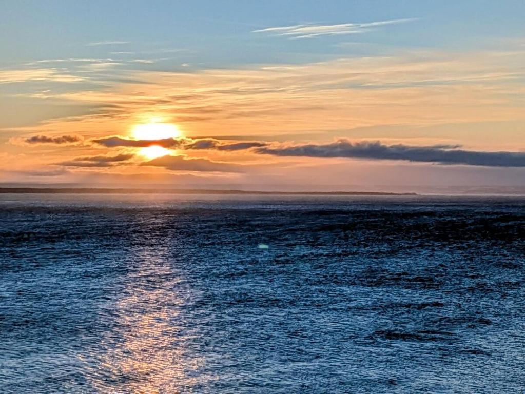 a sunset over the ocean with a trail in the water at Le Repere, Beach, Whales, and Ferry in Saint-Siméon