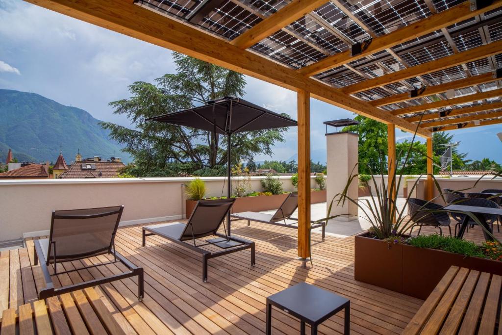a deck with chairs and a table and an umbrella at Wellness Smart Suites in Bolzano