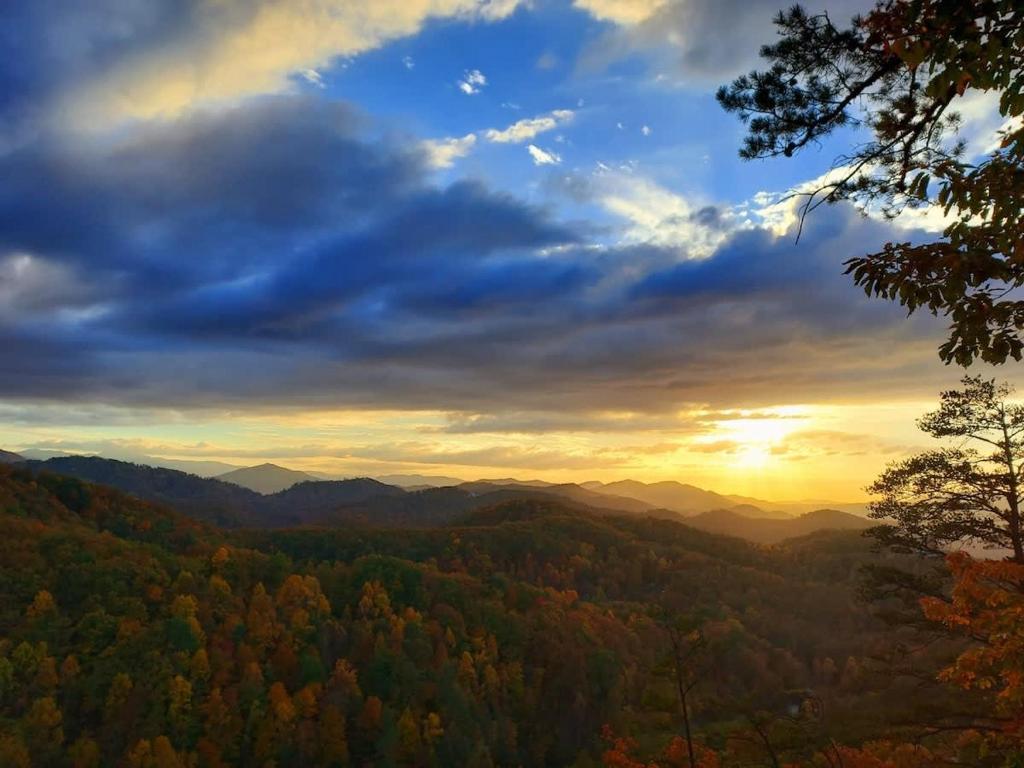a sunset in the mountains with trees in the foreground at The Burrows in Sevierville