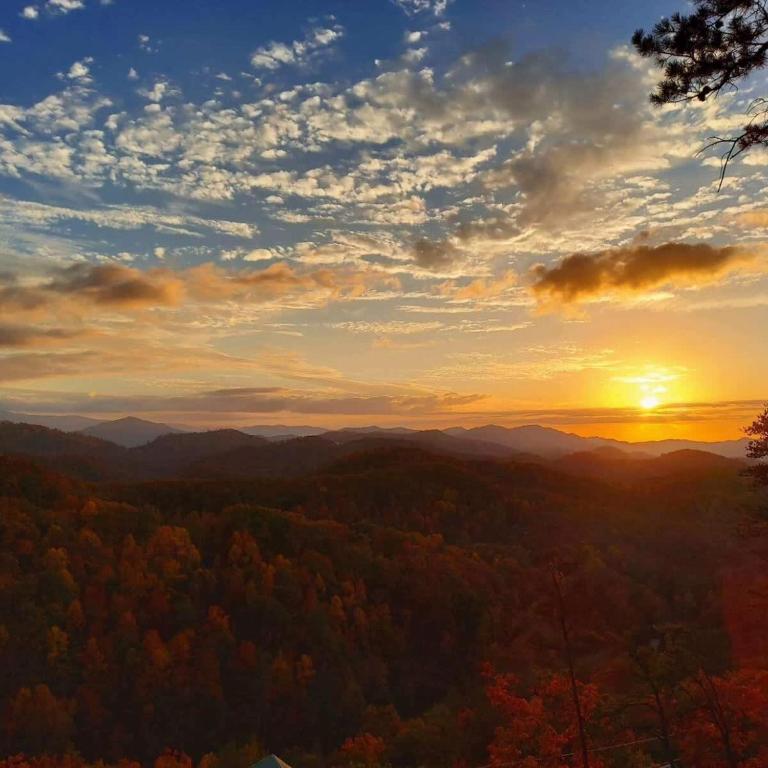 a sunset in the mountains with trees in the foreground at The Rustic Charm in Sevierville