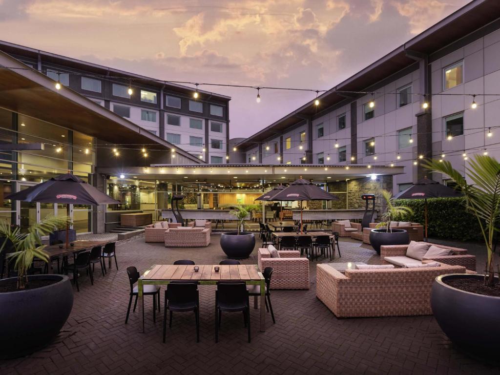 an outdoor patio with couches and tables and umbrellas at Novotel Auckland Ellerslie in Auckland