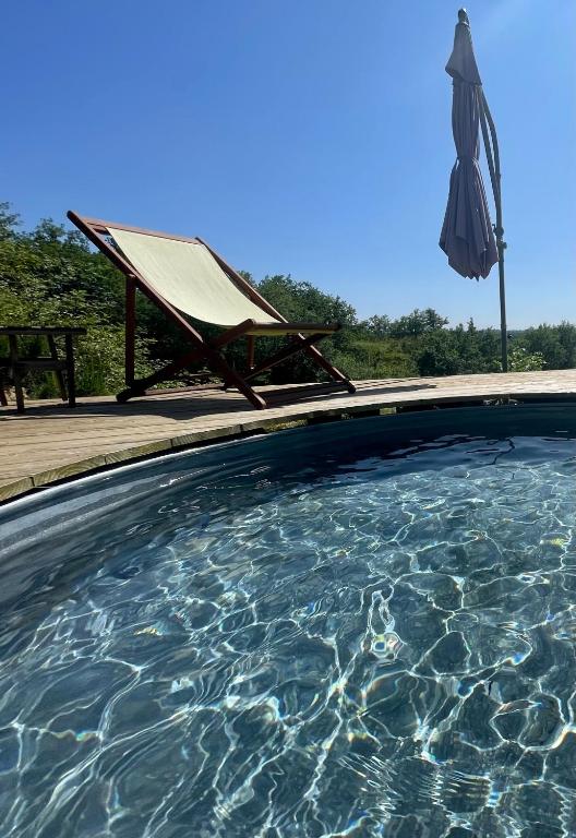 a swimming pool with a hammock and an umbrella at Cabane Bivouac avec échelle à l'ombre des chênes in Idrac-Respailles