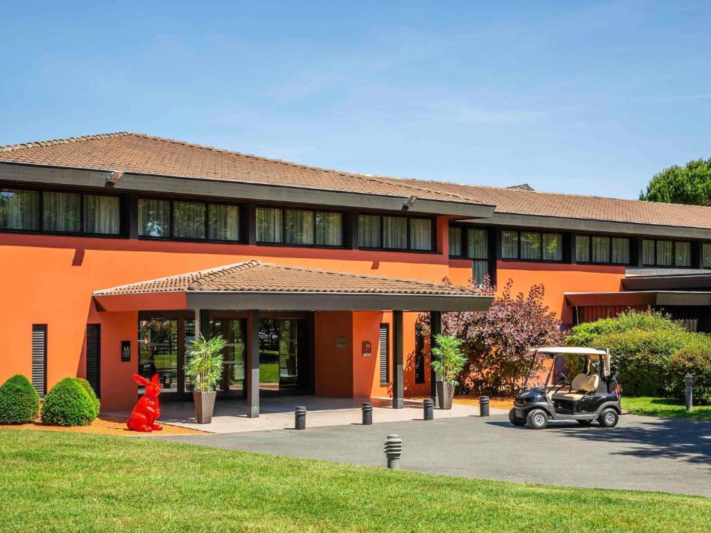 an orange building with a golf cart in front of it at Cabot Hotel Bordeaux - MGallery Collection in Le Pian-Médoc