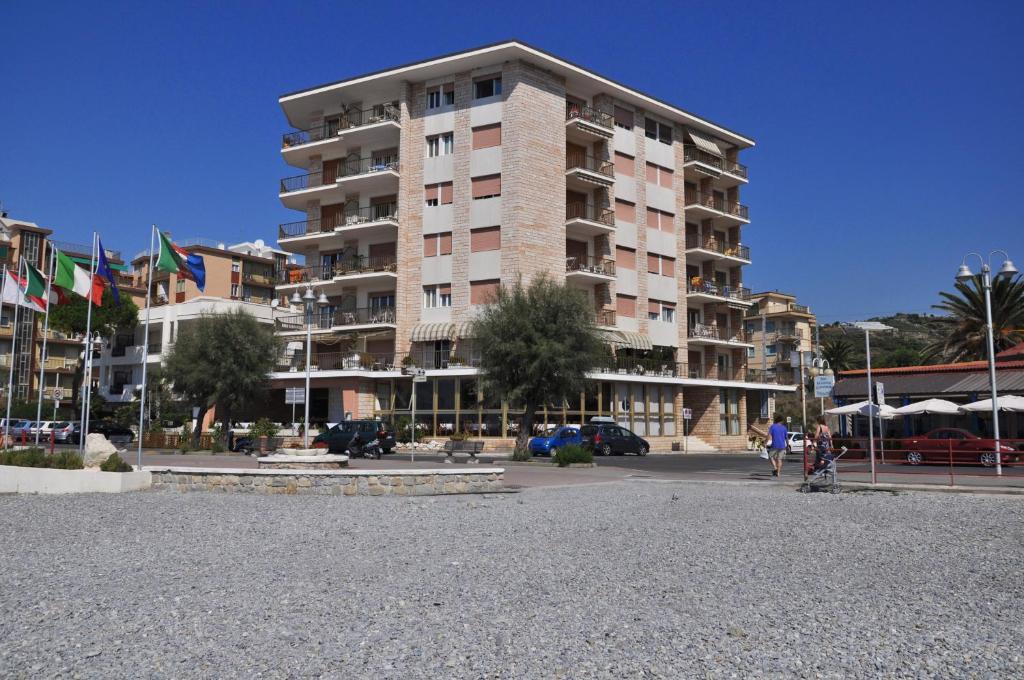 un gran edificio de apartamentos con banderas en un aparcamiento en Gaiavacanze Beach Apartment, en Bordighera