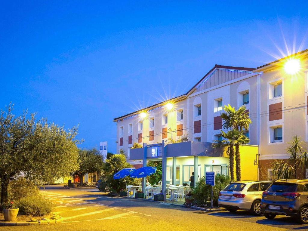 a building with cars parked in a parking lot at Ibis Budget Fréjus Capitou in Fréjus