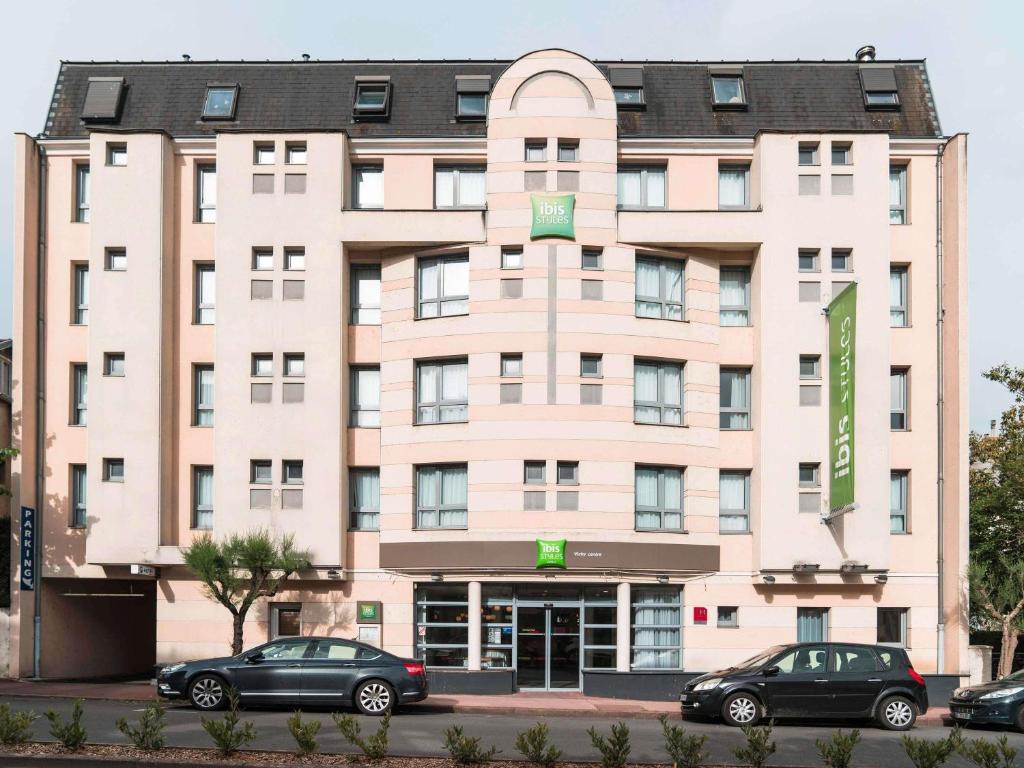 a large pink building with cars parked in front of it at Hôtel ibis Styles Vichy Centre in Vichy