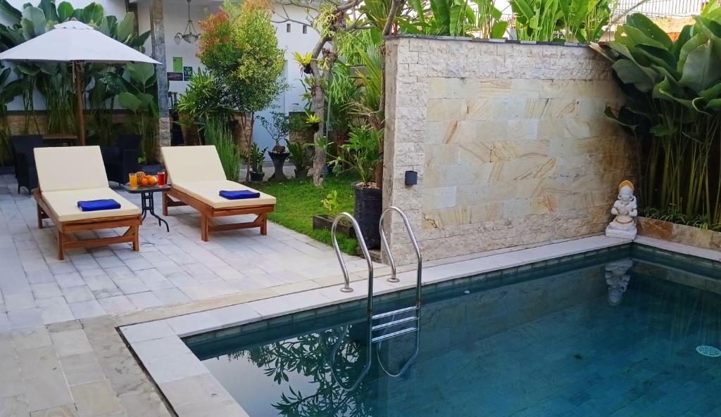 a swimming pool in a backyard with two chairs and an umbrella at VILLA PAPA PUTU in Banjar