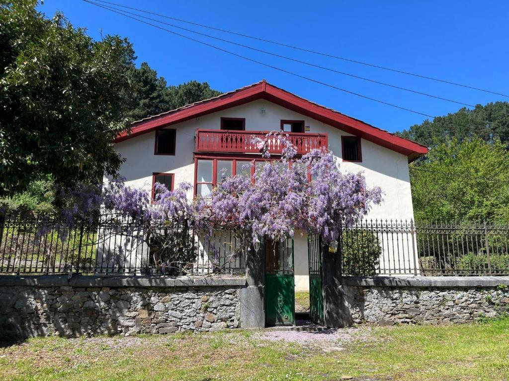 a house with a fence and purple flowers at Lutzin Etxea, Caserío Vasco con piscina, jardín y parking, a 15 min de Bilbao in Llodio