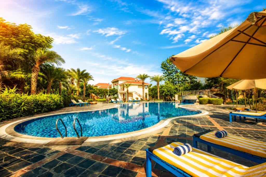 a pool at a resort with two benches and an umbrella at Resort De Coracao - Corbett , Uttarakhand in Rāmnagar