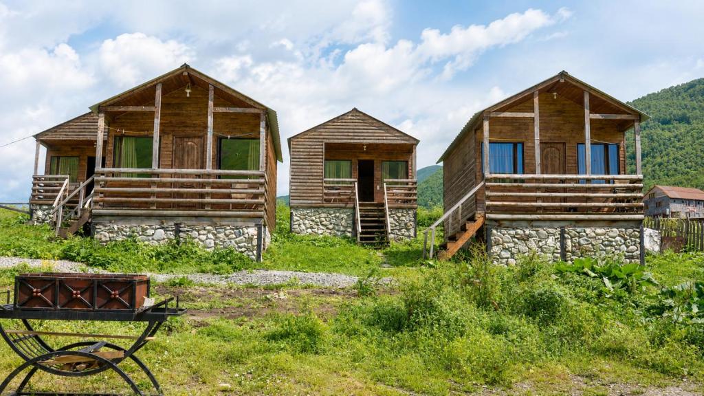 three wooden huts in a field with a cart in front at Ushguli Cabins l Cafe in Ushguli