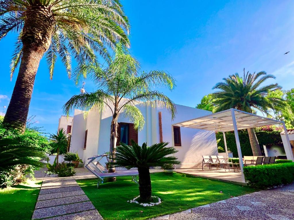 a white house with palm trees and a bench at Villa Almyra - 4 Double Bedrooms with Exclusive Garden & Parking Steps from the Beach in San Vito lo Capo