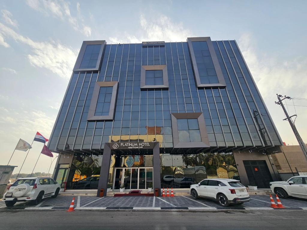 a tall building with cars parked in a parking lot at Basra Platinum Hotel in Al Başrah