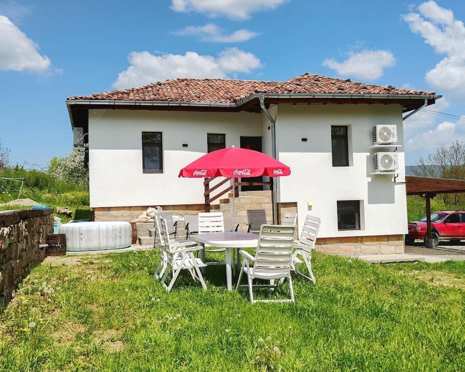 a table with chairs and a red umbrella in front of a house at Bachvarov house Бъчваровата къща in Palitsi
