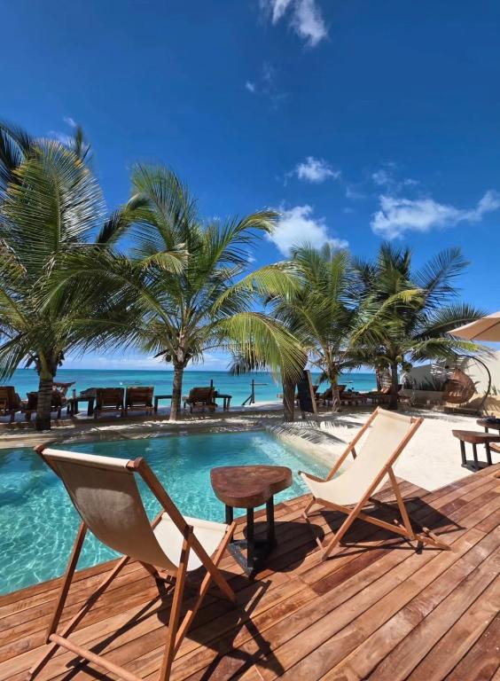 a deck with chairs and a table next to a swimming pool at Tangawizi Lodge Zanzibar - Adults Only in Jambiani