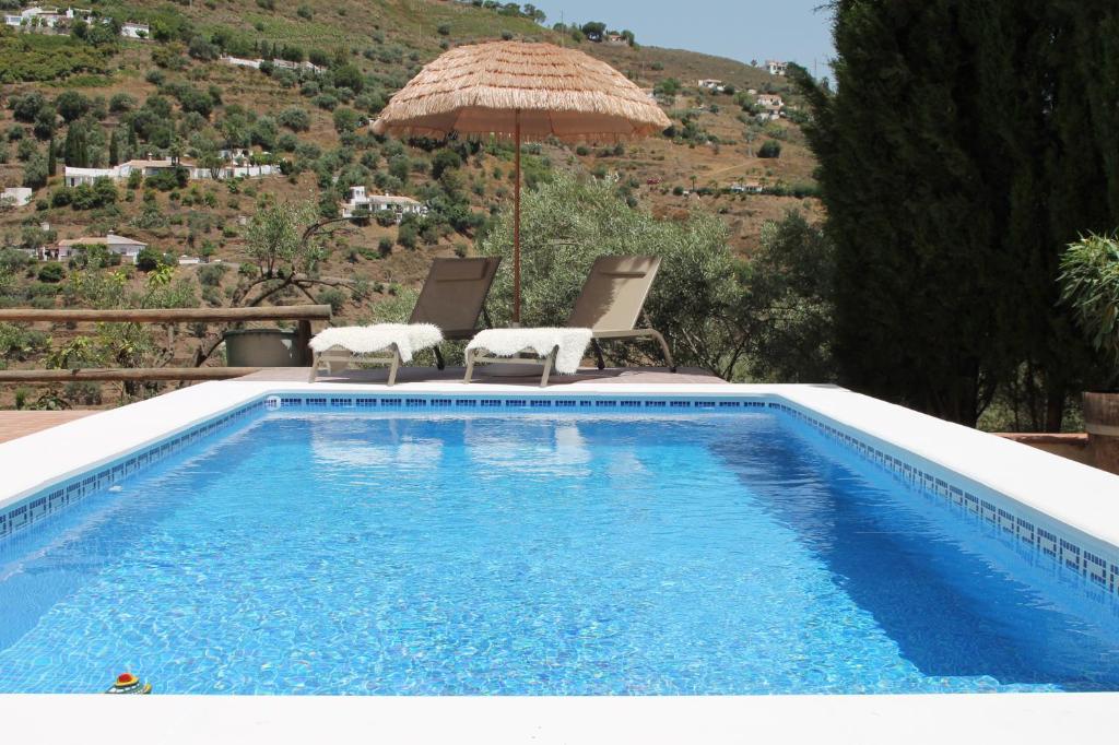 ein Schwimmbecken mit zwei Stühlen und einem Sonnenschirm in der Unterkunft Marimonta in Cómpeta