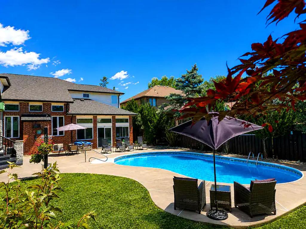 a pool with chairs and an umbrella next to a house at Windsor Luxury Oasis in Windsor