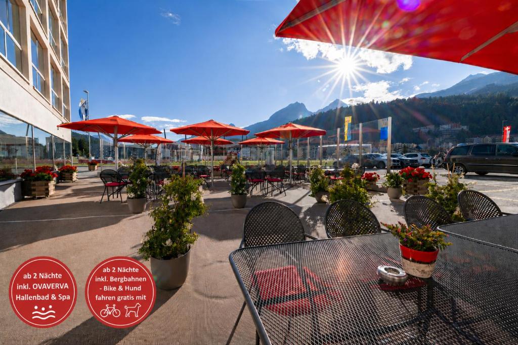 patio ze stołami, krzesłami i czerwonymi parasolami w obiekcie Hotel Sonne St. Moritz 3* Superior w Sankt Moritz