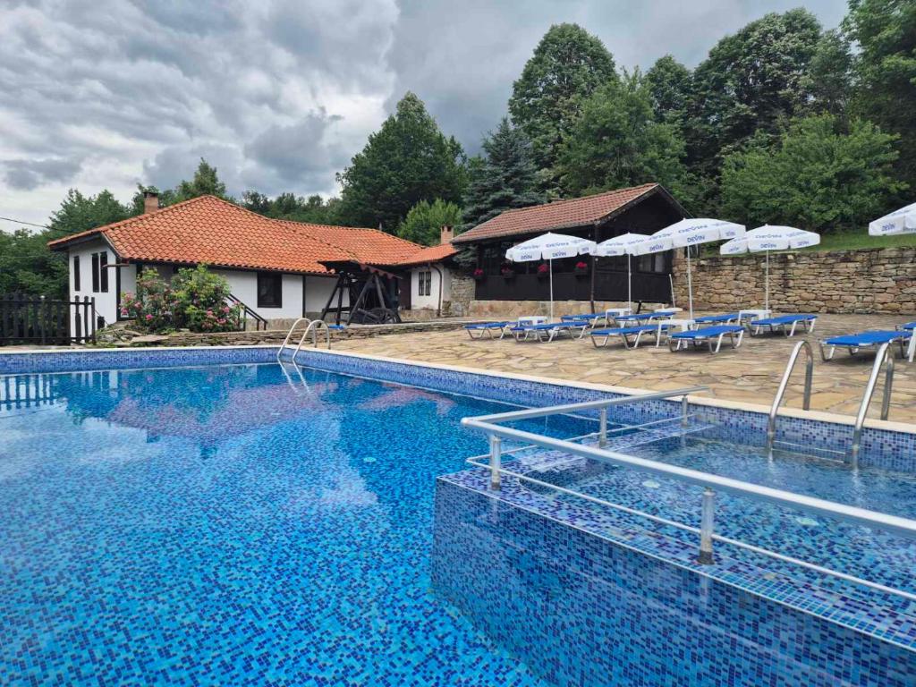 a large blue swimming pool with chairs and umbrellas at Къща Цачеви in Tryavna