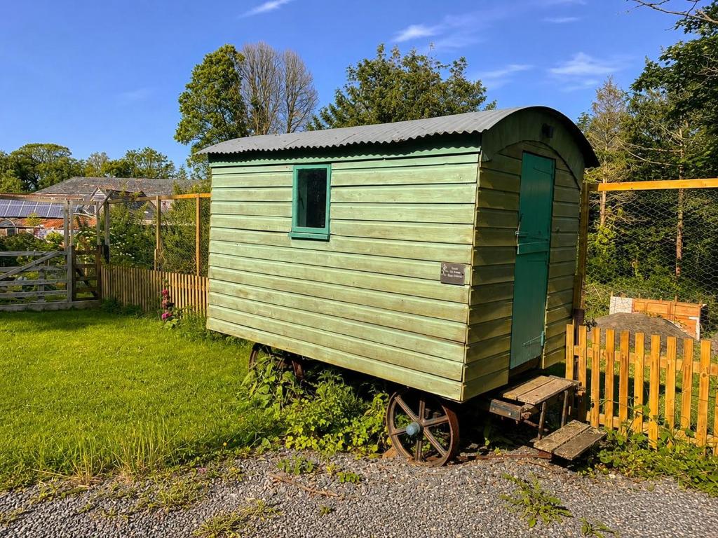 a green shed sitting next to a fence at Mabel the Steam Roller Caravan at Rosuick Organic Farm in Saint Martins Green