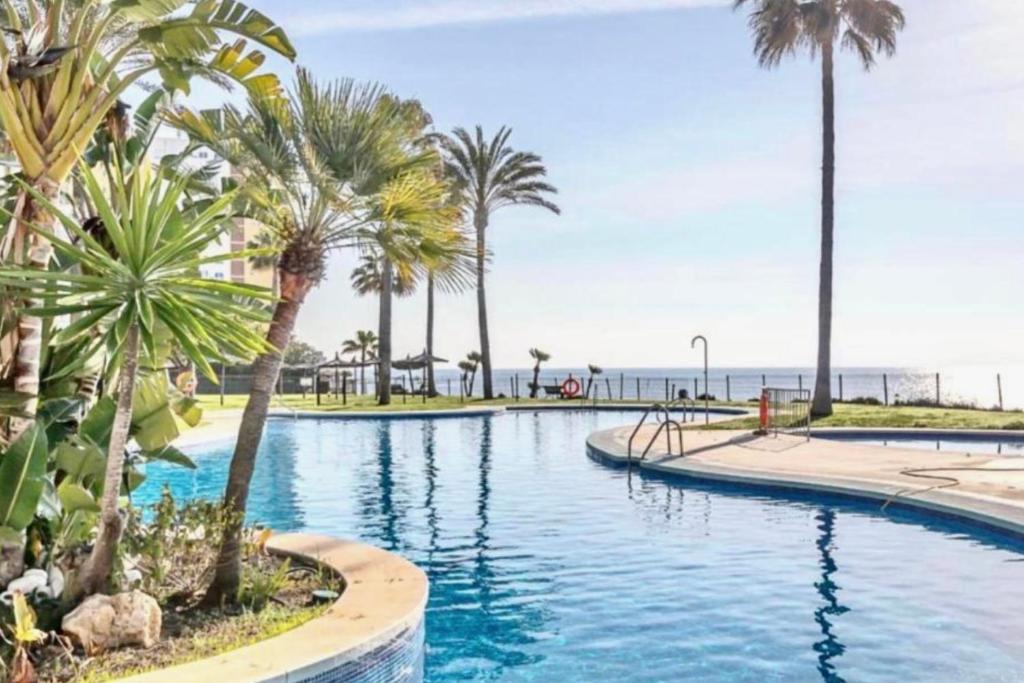 a swimming pool with palm trees and the ocean at MI CAPRICHO BEACHFRONT 410 - Apartment with terrace and private garden by the sea in Mijas Costa