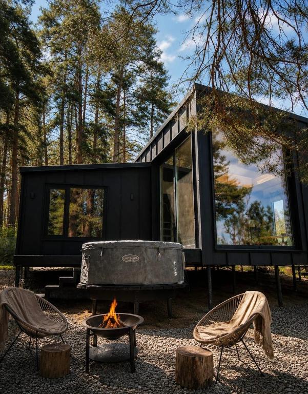 a black tiny house with a fire pit and chairs at Connect Cabin - Bungalow Brasov, jacuzzi & forest view in Purcăreni