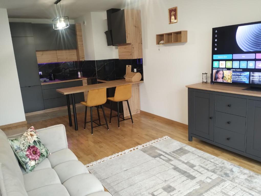 a living room with a couch and a kitchen at Nowoczesny Apartament 400 M Od Plaży Prywatny Ogródek Ełk in Ełk