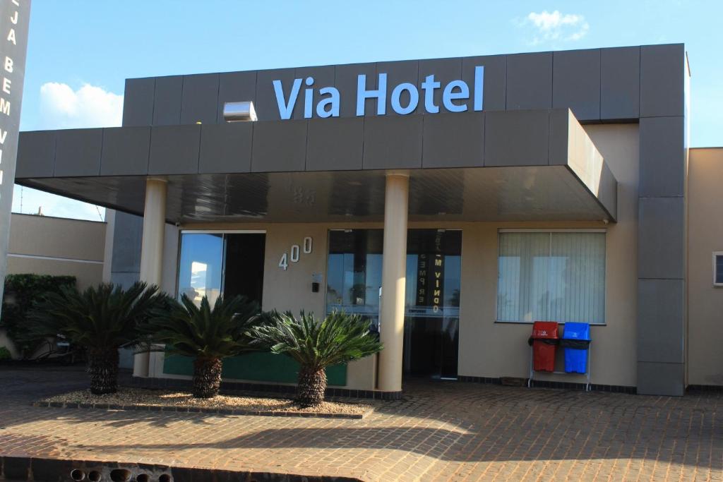 a hotel with palm trees in front of a building at Via Hotel in Monte Alegre de Minas