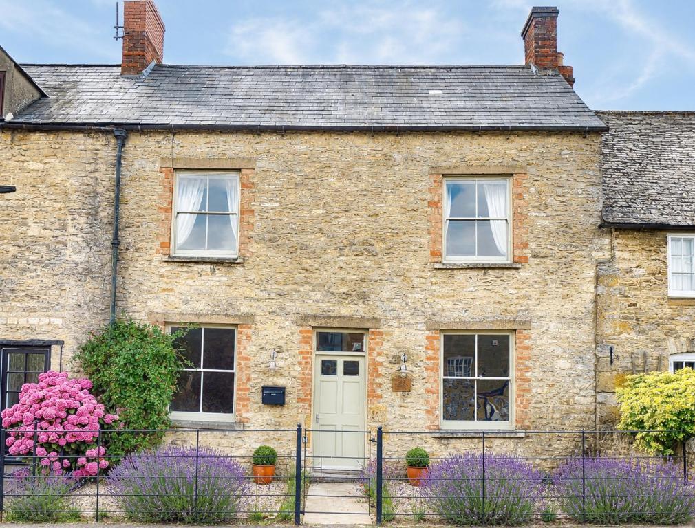 a brick house with purple flowers in front of it at Rathbone Cottage in Stow on the Wold