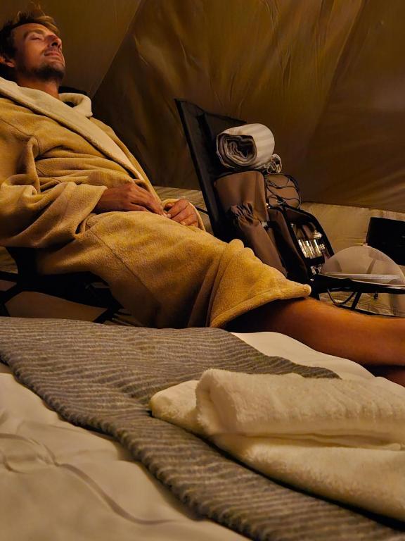 a man laying in a bed wrapped in a blanket at Acorn Creek Tented Camp in Nidda