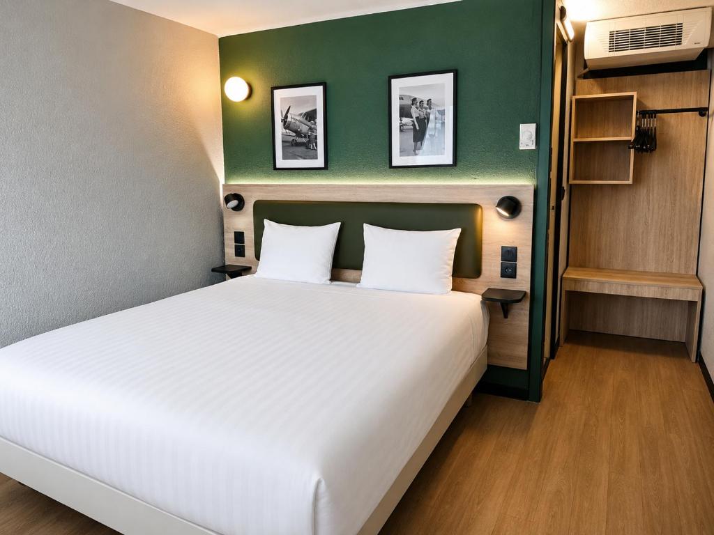 a bedroom with a large white bed with a green wall at Kyriad Direct Le Bourget Gonesse in Gonesse