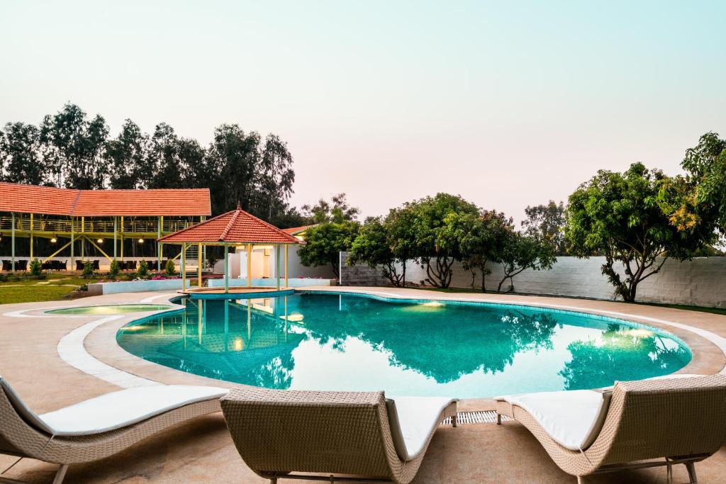 a swimming pool with two chairs and a building at Fiestaa Resort n Events Venue in Devanhalli