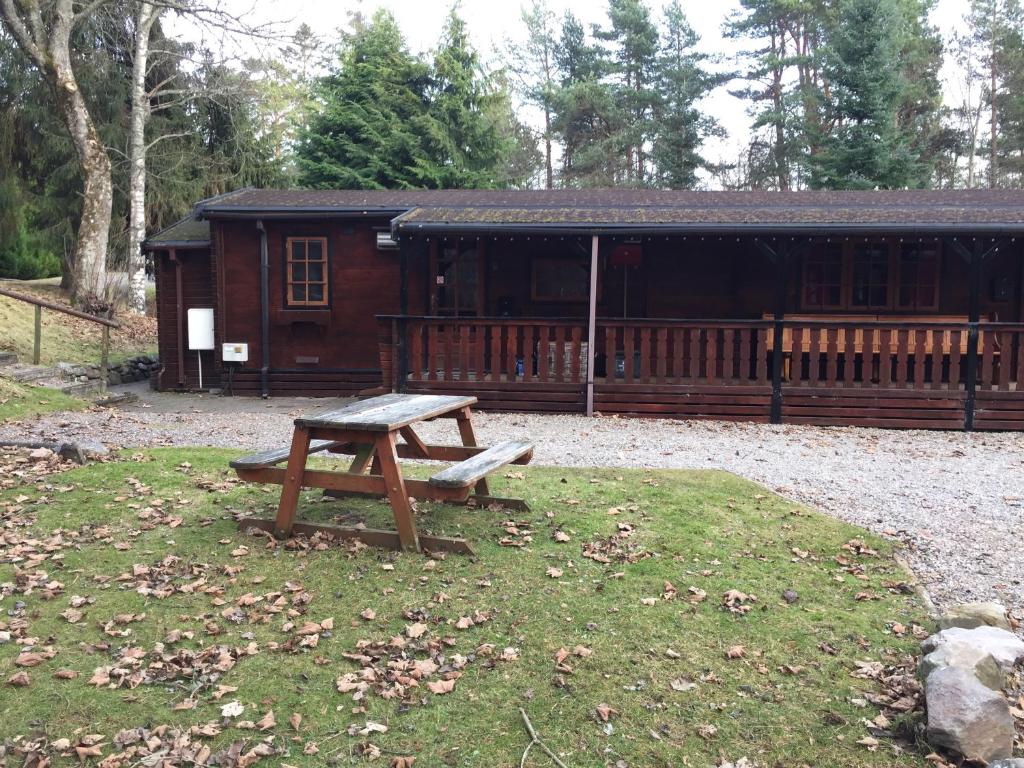 a wooden cabin with a picnic table in the grass at Lurchers Cabin Aviemore in Aviemore