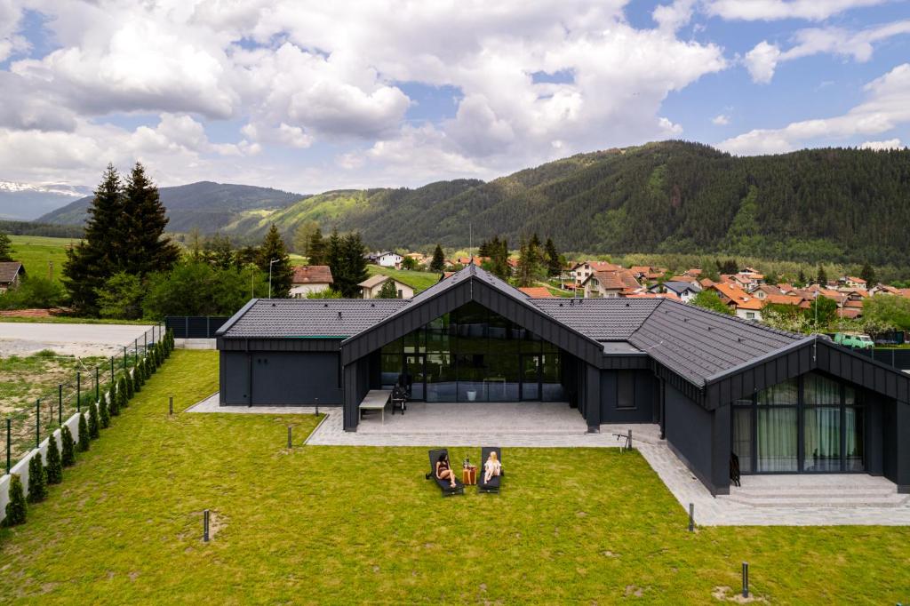 two people sitting on the grass in front of a black house at Chalet Rila in Govedartsi