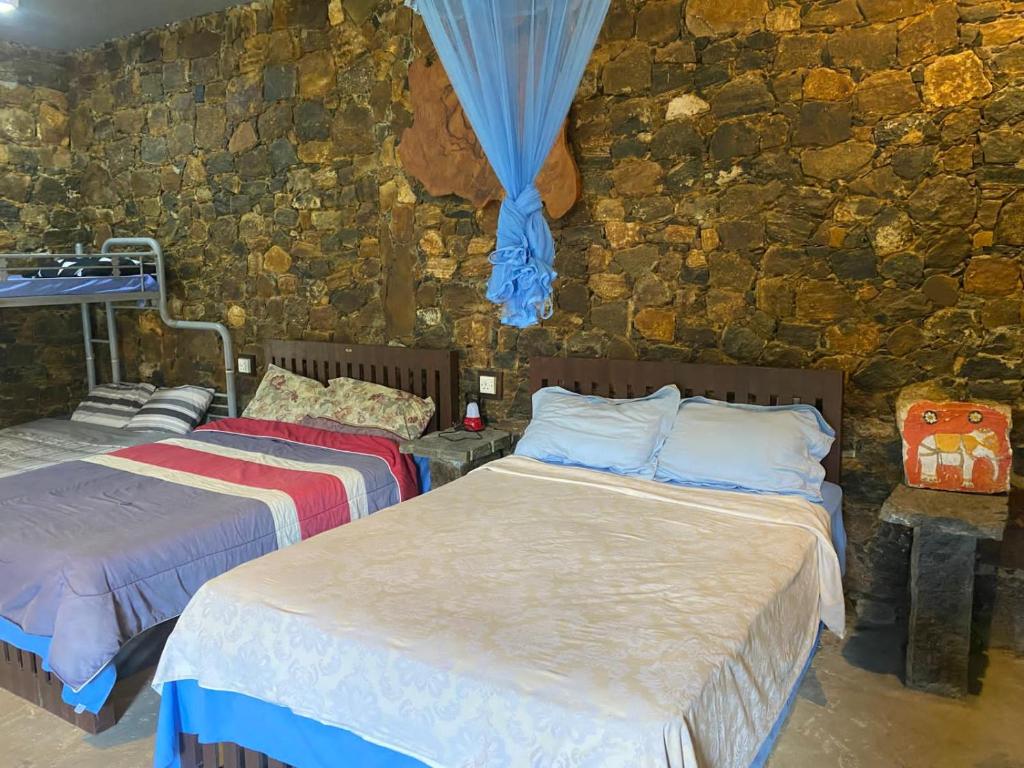 two beds in a room with a stone wall at Misty mountains residents in Huluganga